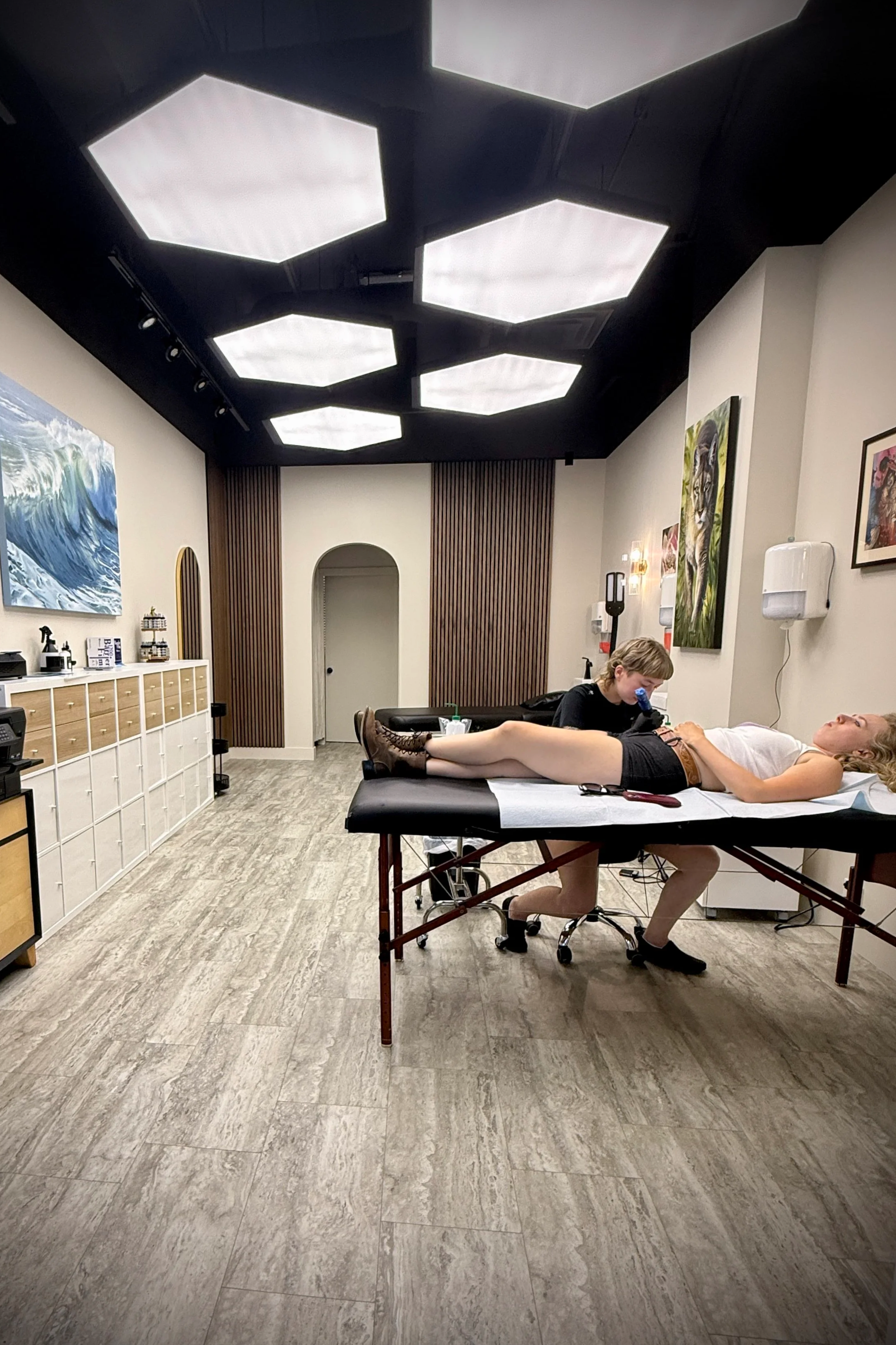 The Ember Studio interior, lit by signature hexagonal ceiling lights, during a tattoo session